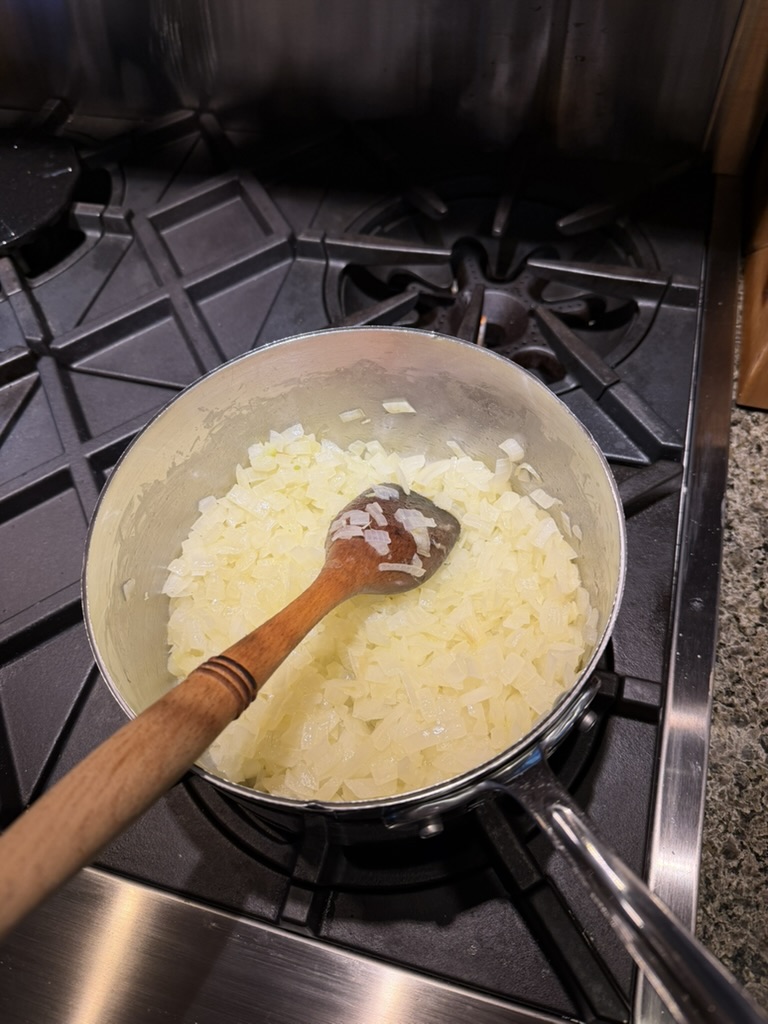 Chopped yellow onions sweating in a pot with a wooden spoon