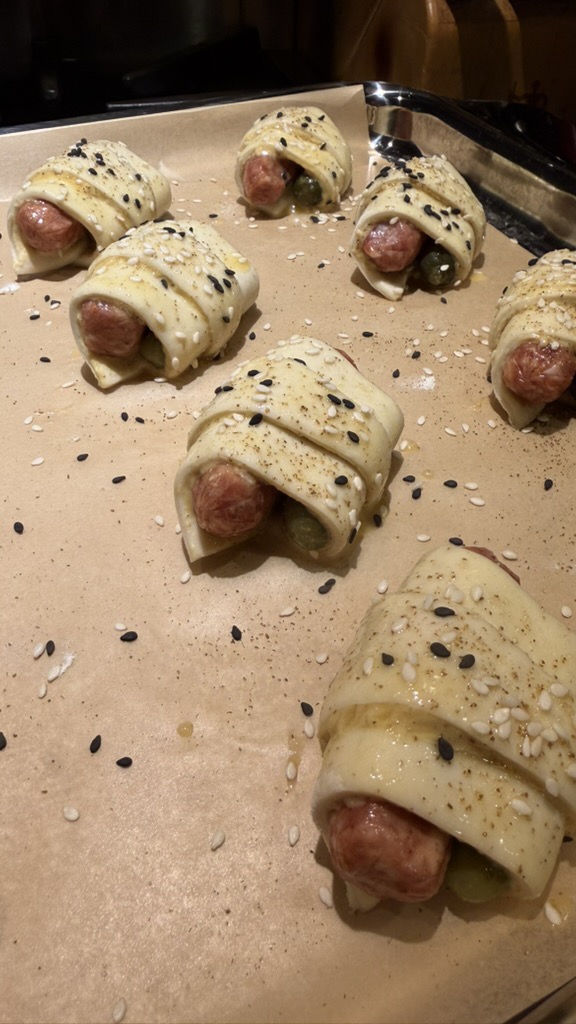 Rolled pigs in a blanket on parchment-lined tray with egg wash and sesame seeds